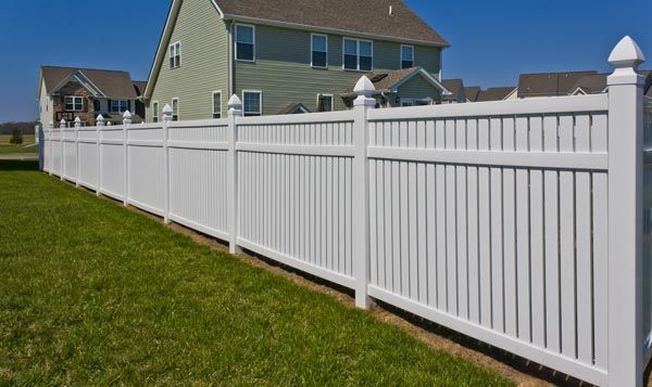 White vinyl fence along a grassy suburban yard beside houses on a sunny day