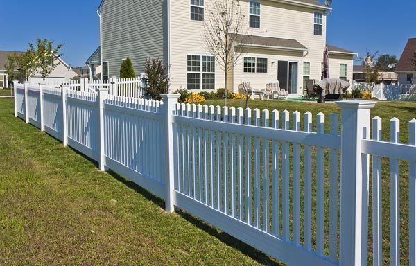 White vinyl fence lining a suburban yard beside a beige house on a sunny day