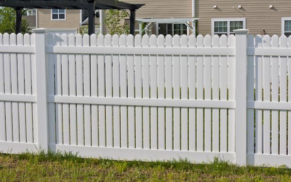 White vinyl picket fence in front of suburban houses and a grassy yard