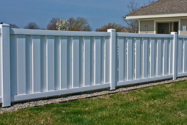 White vinyl fence along a grassy yard beside a house under a blue sky