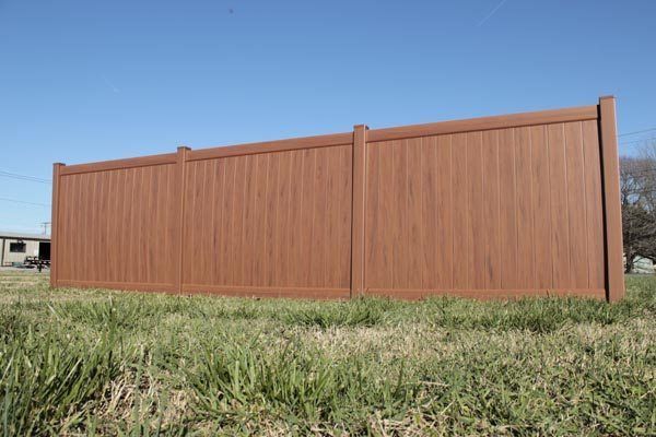 Tall brown wooden privacy fence in a grassy field under a clear blue sky