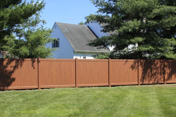 Backyard with green lawn, wooden privacy fence, and a house partly visible behind trees