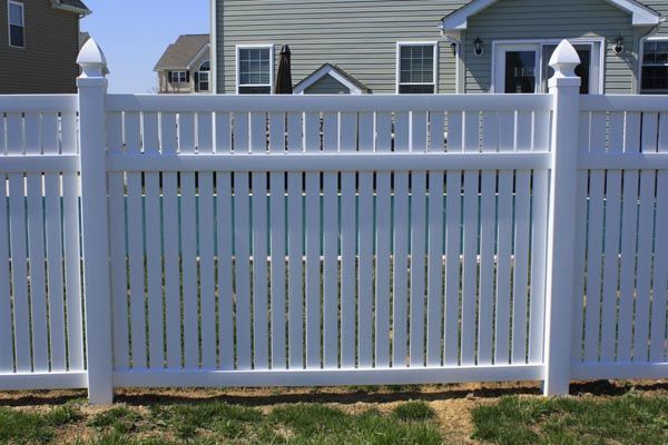 White vinyl picket fence in front of a suburban house and lawn