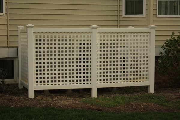 White lattice porch skirt beneath beige house siding, with a small window above and grass below