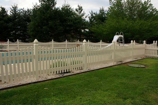 White picket fence around a backyard pool with lawn and trees in the background