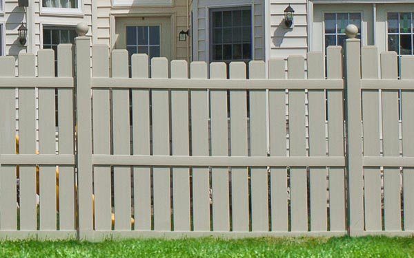 White wooden fence in front of a house exterior with windows and wall-mounted lights.