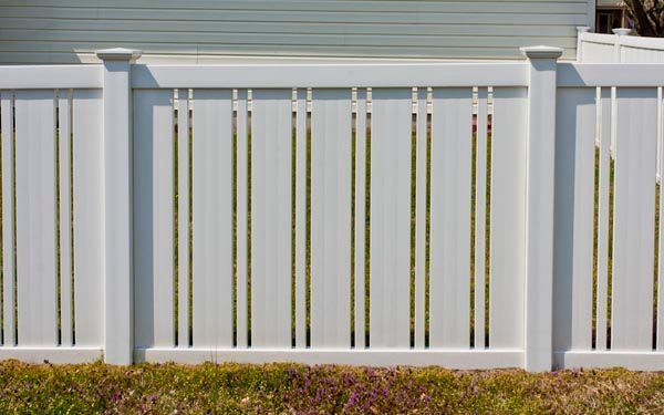 White vinyl privacy fence with vertical slats and beige posts in front of a house.