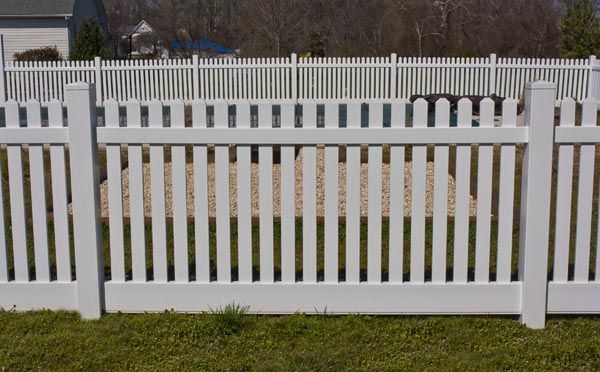 White picket fence with vertical slats in front of a grassy yard and another fence in the background