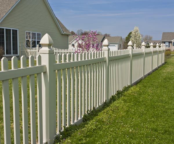 White picket fence beside a green lawn and suburban house under clear blue sky