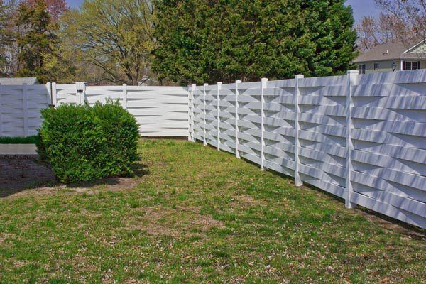 Backyard with white vinyl fence, green lawn, and a trimmed shrub under bright daylight