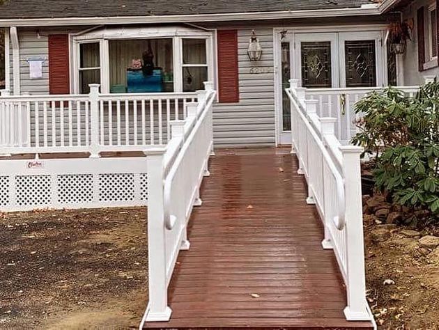 Front walkway and ramp leading to a house with white railings and a brown deck.