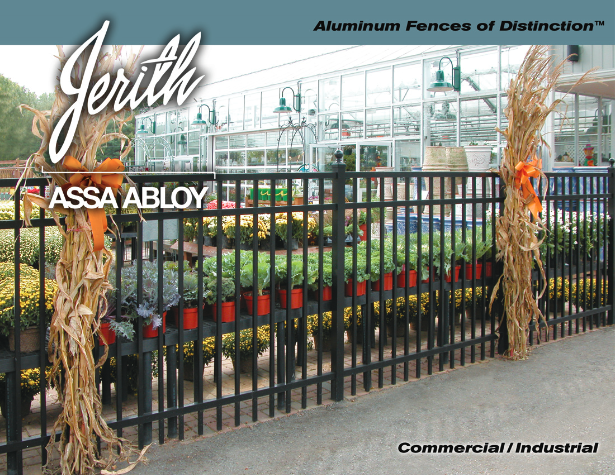 Black metal fence with decorative tan aluminum posts in front of a greenhouse and plants.