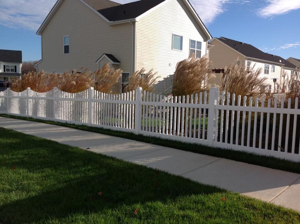 Suburban house with white picket fence beside a sidewalk and green lawn