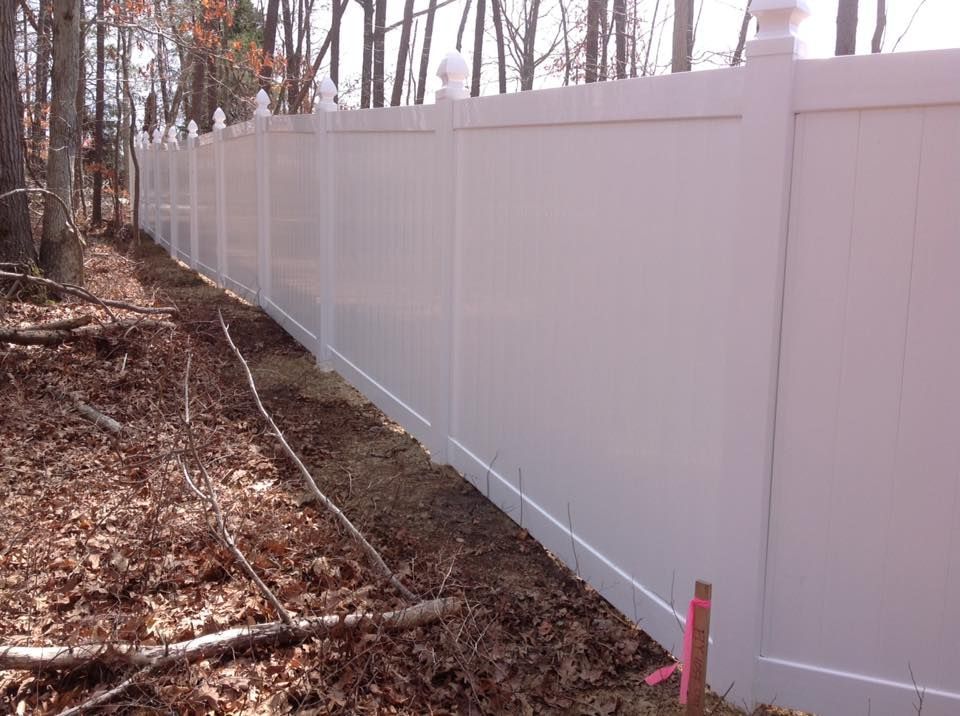 White vinyl fence along a wooded, leaf-covered yard in autumn