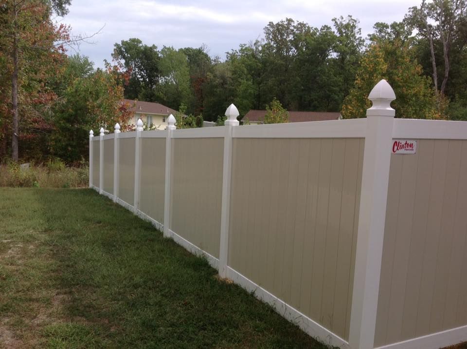 White vinyl privacy fence along a grassy yard with trees in the background