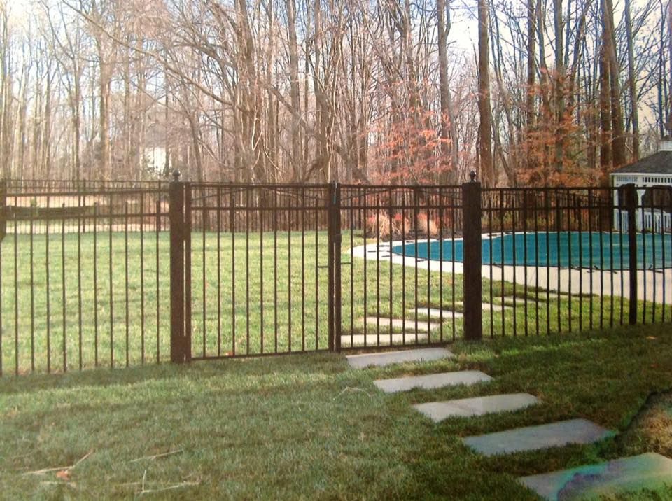 Backyard with black metal fence, grass, stepping stones, and an above-ground pool near leafless trees