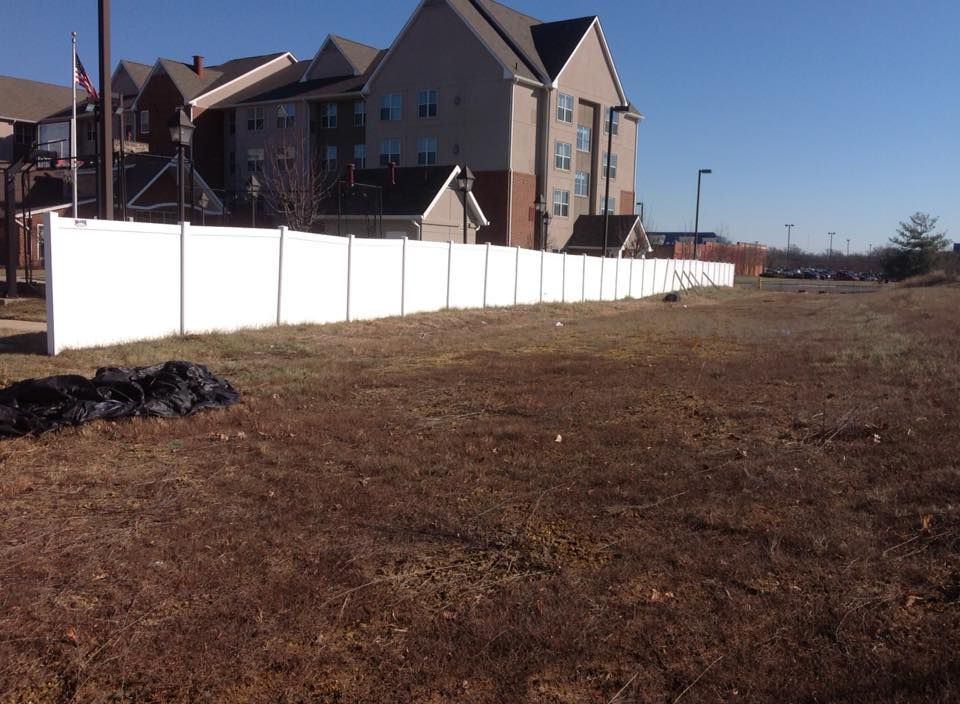 Apartment buildings beside a white fence along a grassy, open lot under a clear blue sky