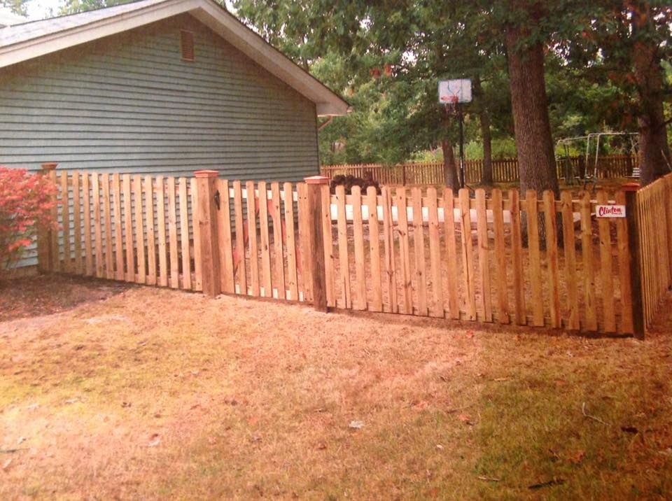 Wooden fence with a gate beside a house and trees in a yard