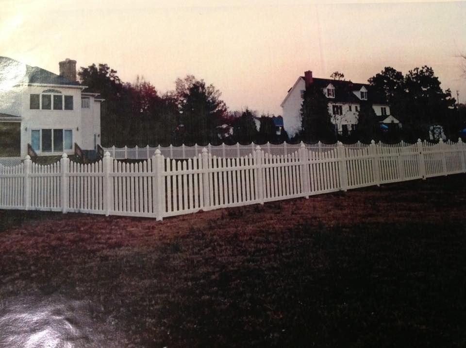 White picket fence beside houses at dusk, with trees and a cloudy pink sky.
