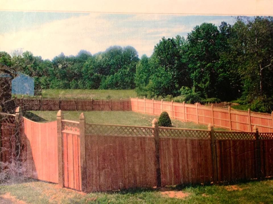 Wooden fenced backyard with a grassy yard, surrounded by trees under a cloudy sky