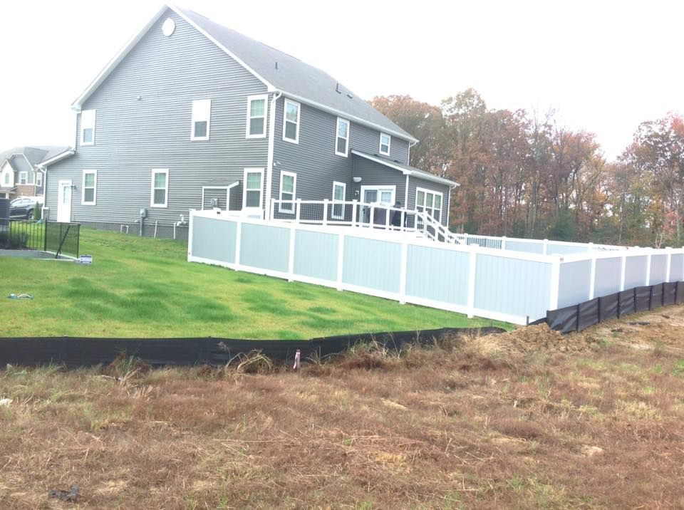 Gray house with white fence and ramp in a grassy yard, with autumn trees in the background