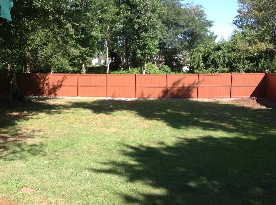 Sunny backyard with green lawn, red fence, and tall trees casting shade