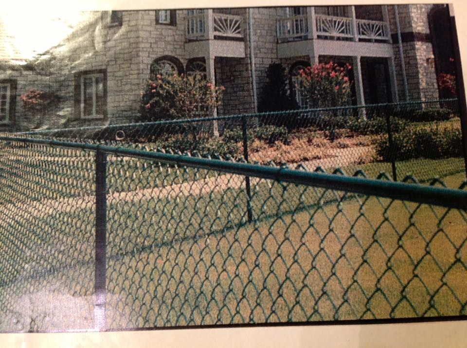 Stone apartment building behind a green chain-link fence and courtyard shrubs