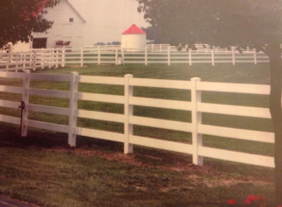 White split-rail fence around a grassy field with a small red-roofed gazebo in the distance