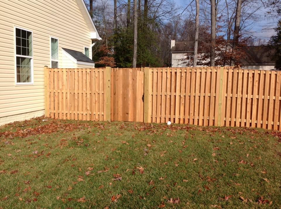 New wooden fence beside beige house in a grassy yard with fallen leaves