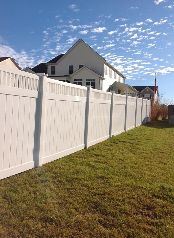 White privacy fence beside a grassy yard under a blue sky with scattered clouds