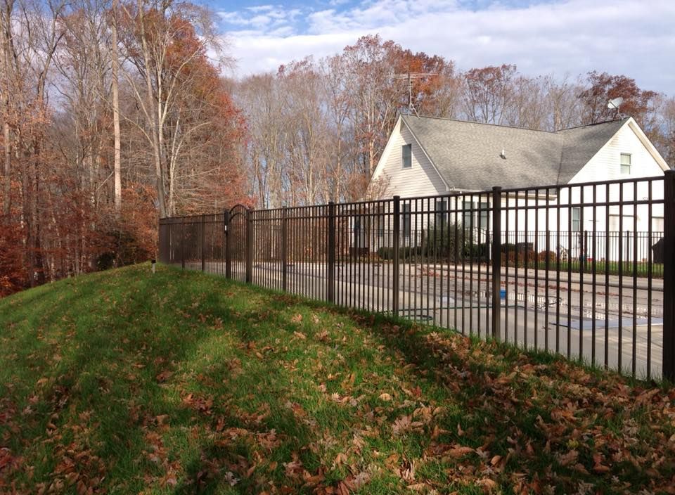 Black metal fence along a grassy slope beside a white house and autumn trees