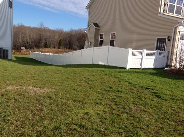 Backyard with white vinyl fence beside beige house and green lawn under blue sky