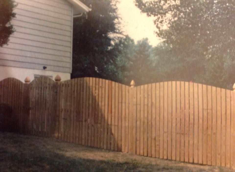 Wooden privacy fence with curved top beside a house in a backyard at dusk
