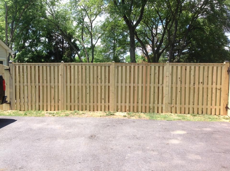 Wooden privacy fence beside a paved driveway, with trees in the background.