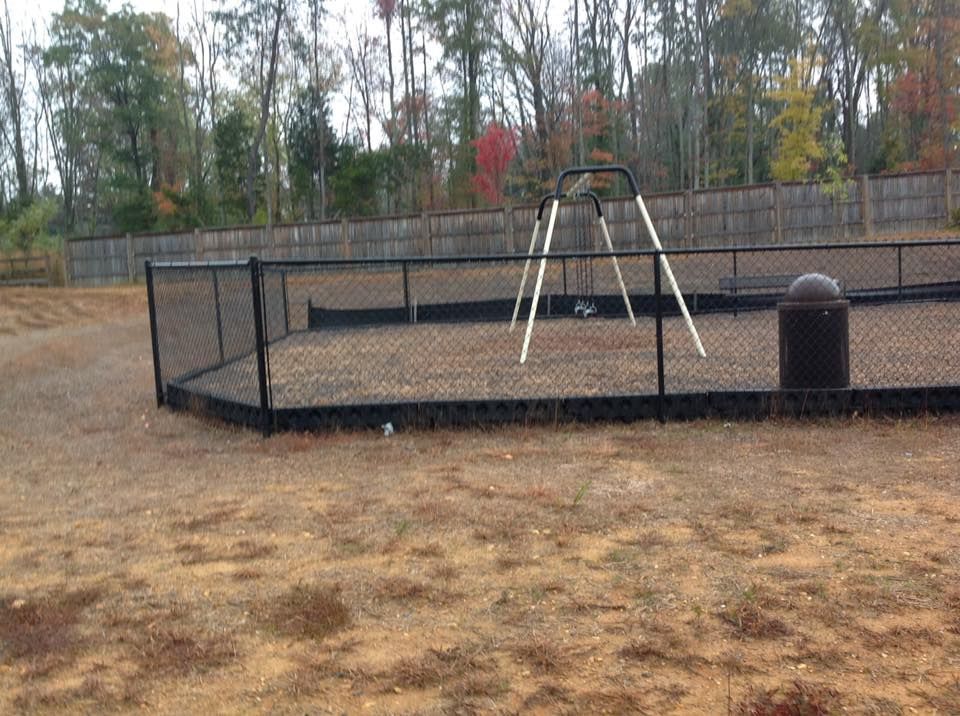Empty fenced playground with swing set and trash can on a dry field under cloudy trees