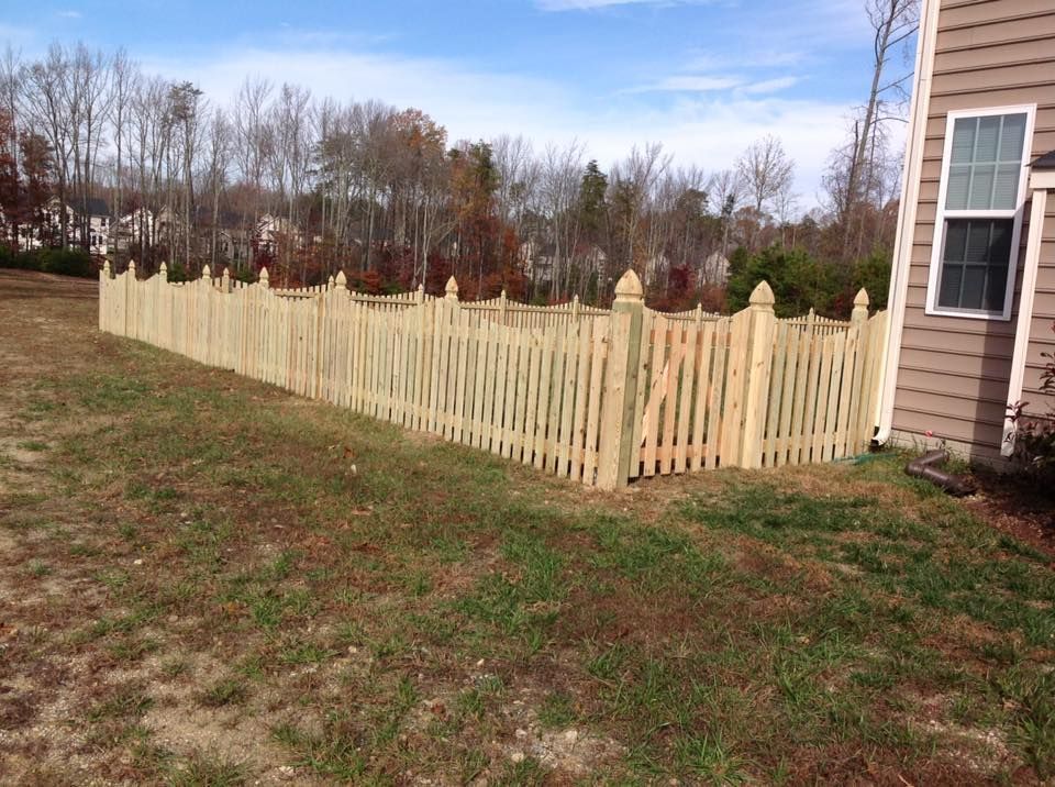 Light tan wooden picket fence along a yard beside a house under a cloudy sky.