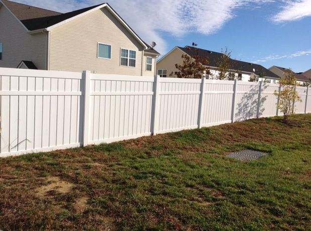 White vinyl fence along a grassy backyard beside beige houses under a partly cloudy sky