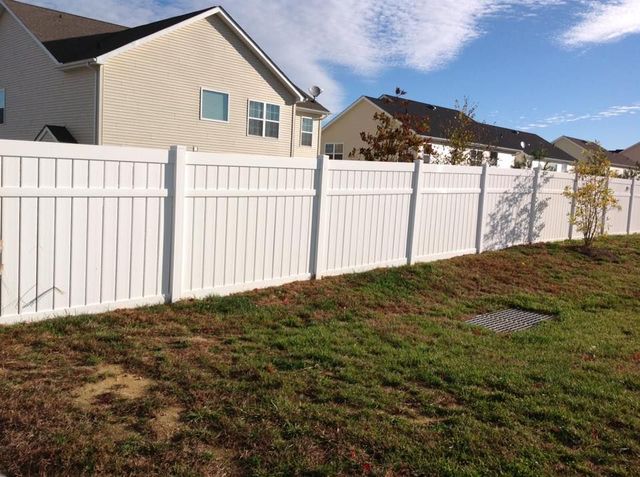 White vinyl fence along a grassy backyard beside beige houses under a partly cloudy sky