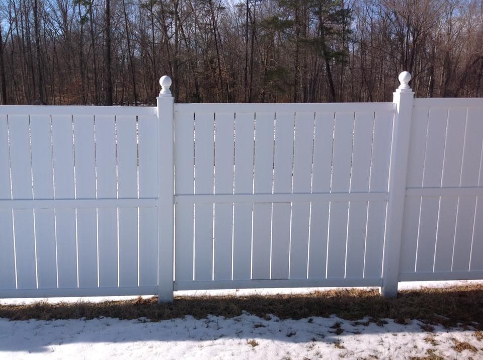 White vinyl fence with posts beside a snowy yard and bare trees in the background