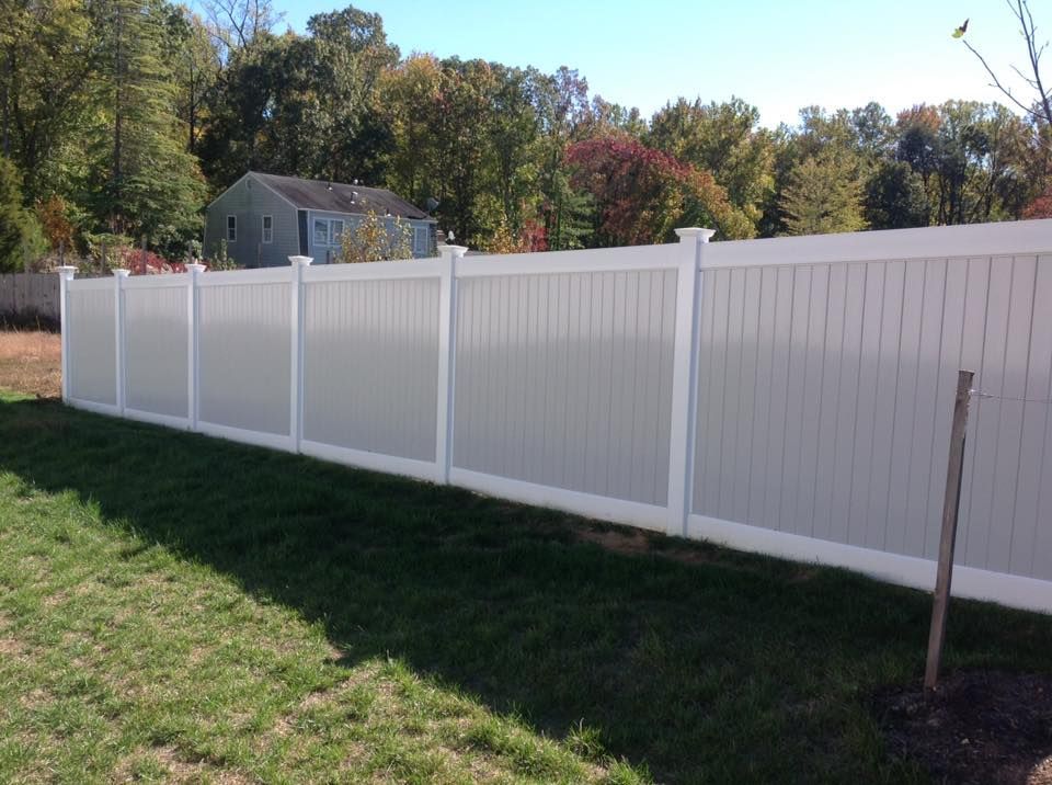 White vinyl privacy fence along a grassy yard with trees and a house in the background