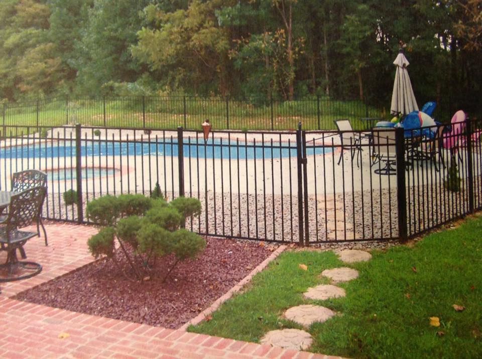 Backyard pool with black fence, patio chairs, and umbrella beside a brick-and-grass walkway
