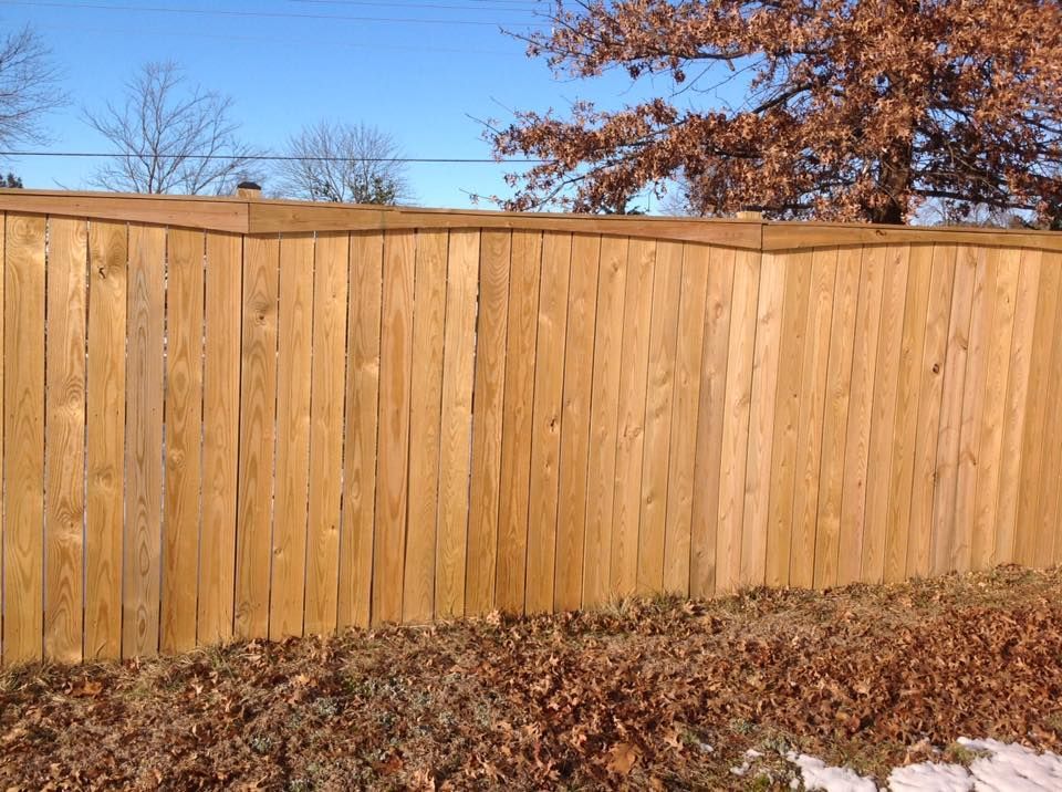 Wooden privacy fence with autumn leaves along the base under a clear blue sky.