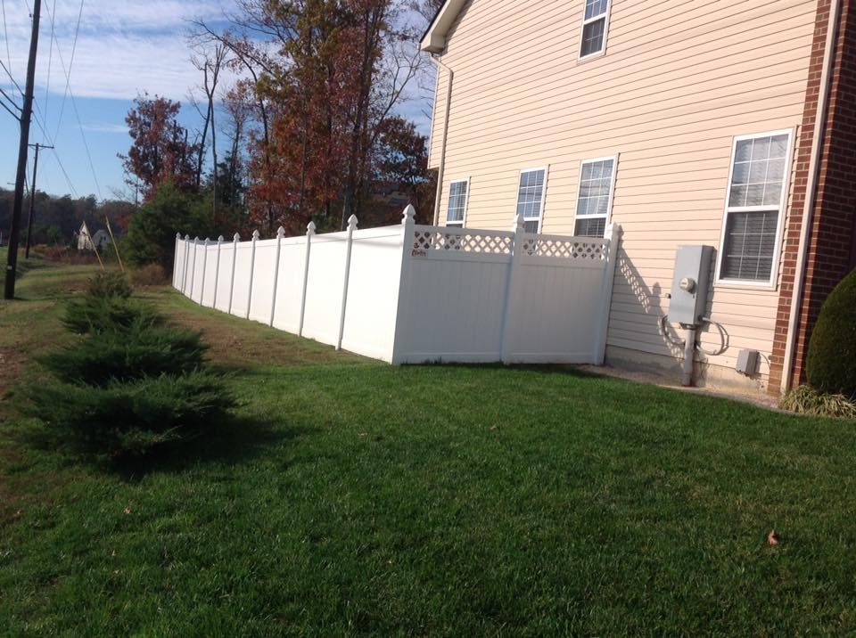 White fence along a grassy side yard beside a beige house on a sunny day
