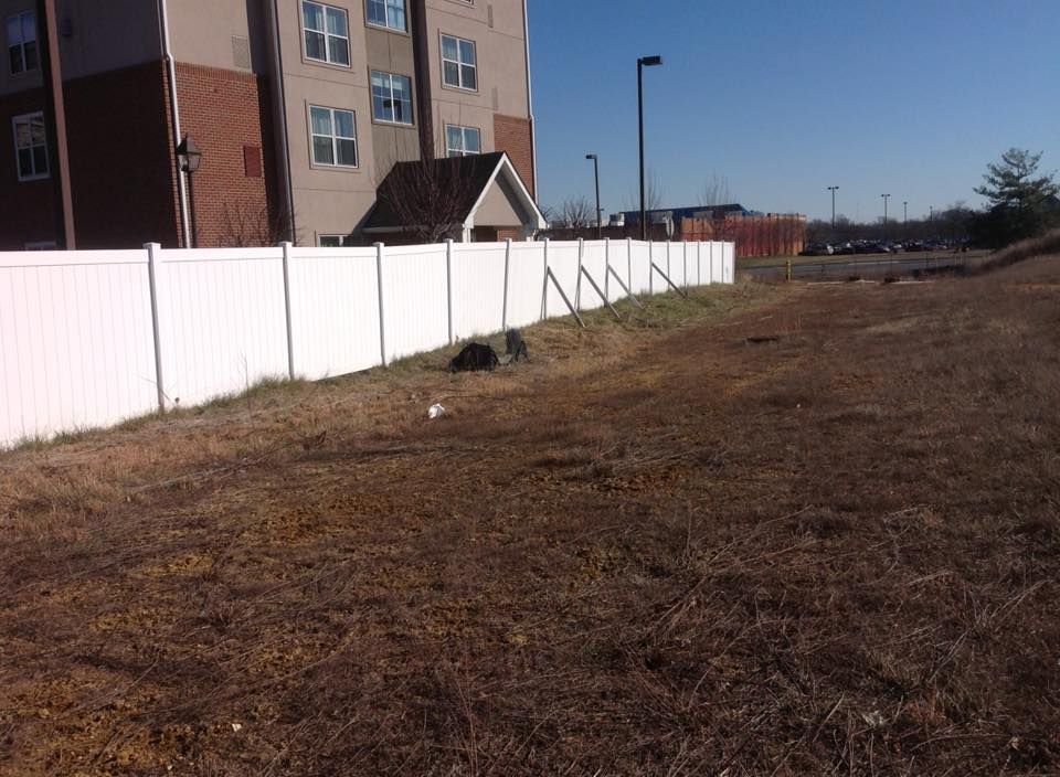 White fence beside a brown grassy lot next to apartment buildings under a clear sky