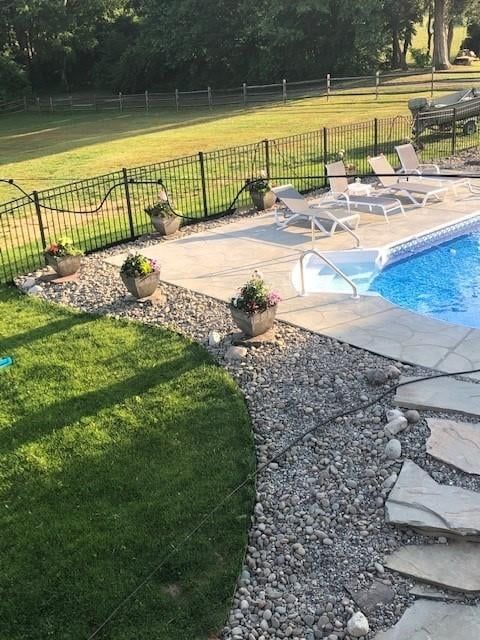 Backyard pool with lounge chairs, stone patio, and green lawn by a black fence