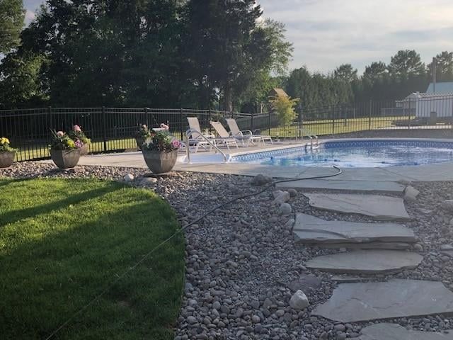 Backyard pool with stone stepping path, flower pots, lounge chairs, and trees at sunset