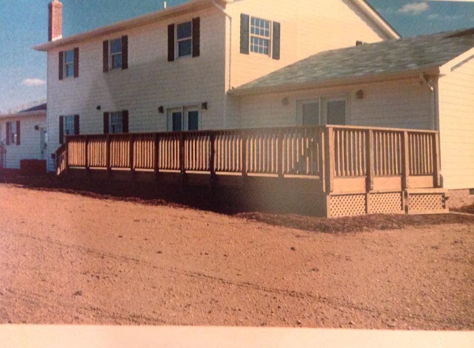 Two-story beige house with a wooden deck and garage on a gravel lot in warm sunlight