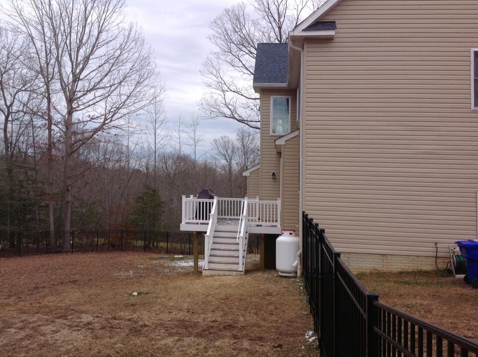 Backyard view of a beige house with a small white deck, stairs, and black fence under cloudy skies