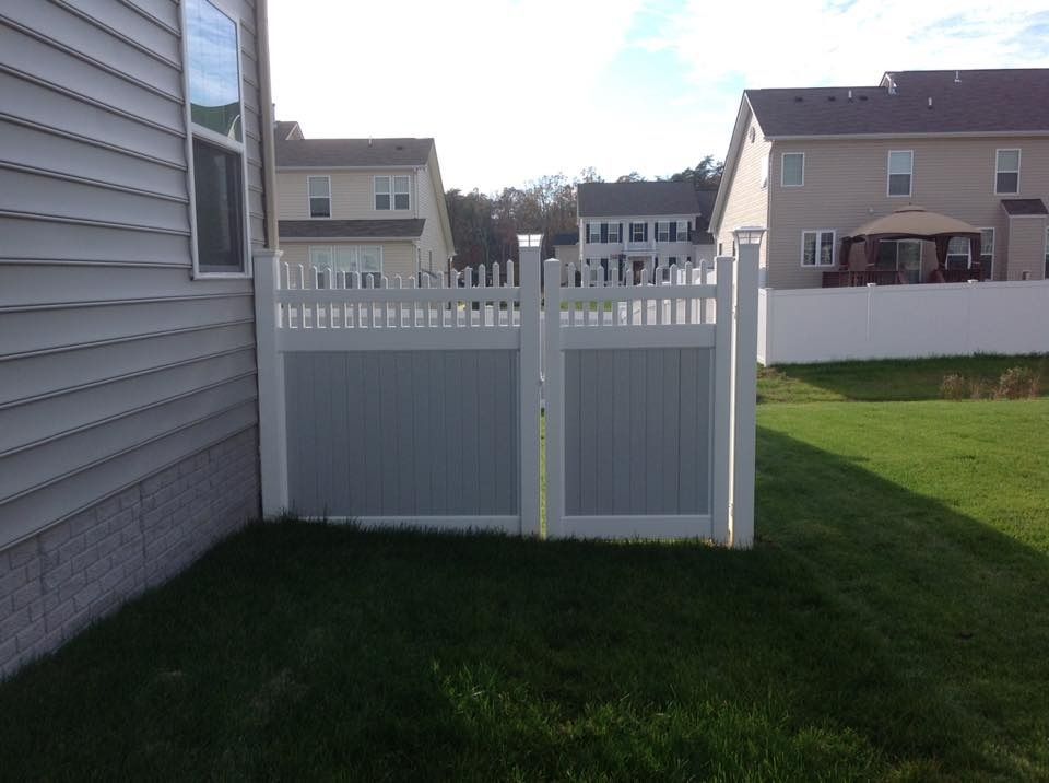 White vinyl fence and gate beside a house in a grassy backyard.