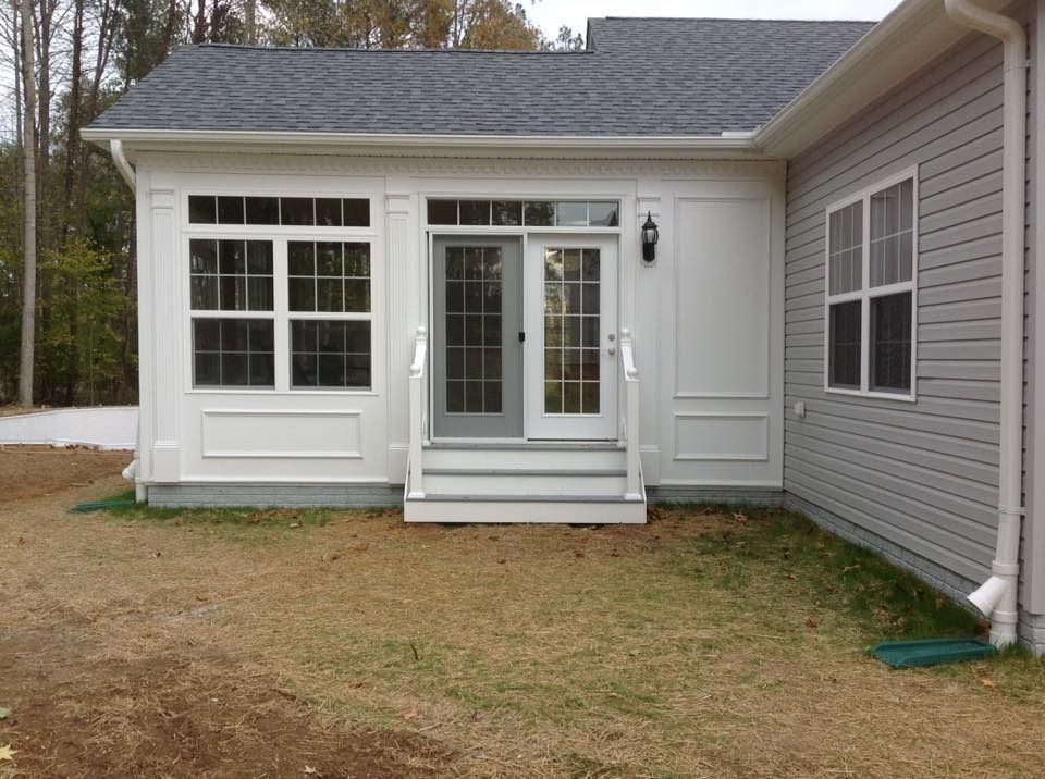 White house exterior with a small porch, front windows, and double glass doors next to gray siding.